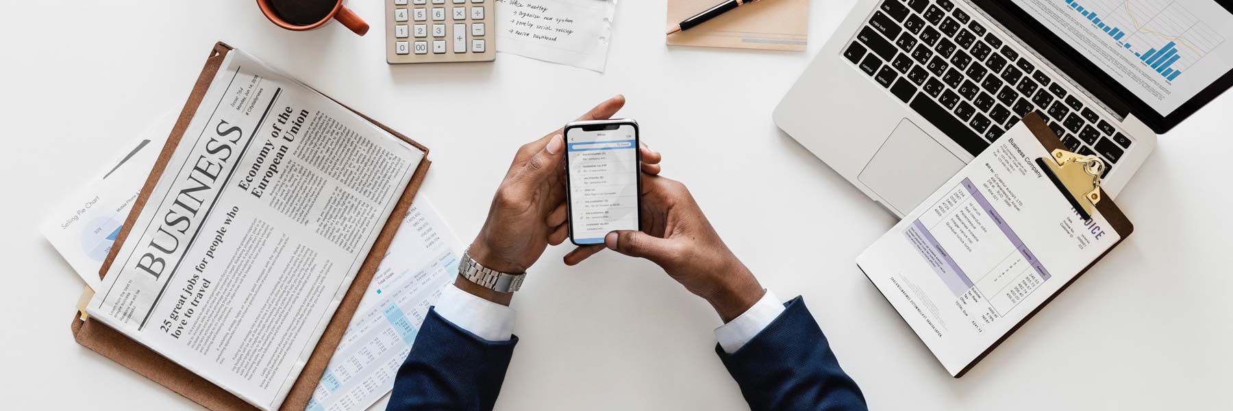 Businessman working through business documents on his cellphone with scattered documents